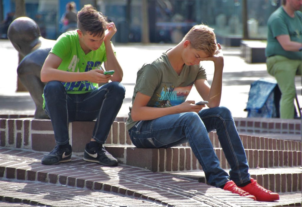 deux enfants assis jouent à des jeux vidéo sur leurs téléphones en plein air