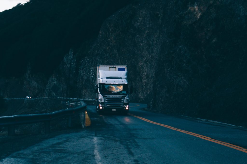 camion scania blanc noir circulant sur route montagne avec parois rocheuses