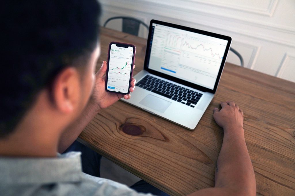 homme consultant des graphiques boursiers sur smartphone et ordinateur portable pour le trading