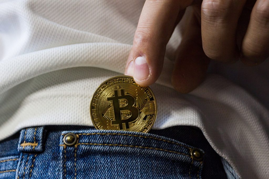 personne tenant une pièce bitcoin dorée au-dessus d'un jean