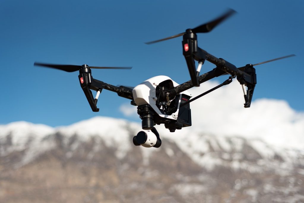 drone blanc et noir en vol avec rotors déployés, montagnes enneigées en arrière-plan