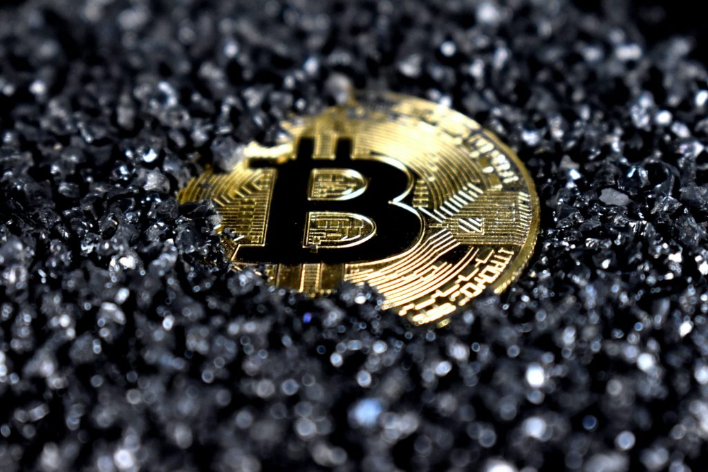 pièce bitcoin dorée sur fond de poussière noire symbolisant le trading de cryptomonnaies