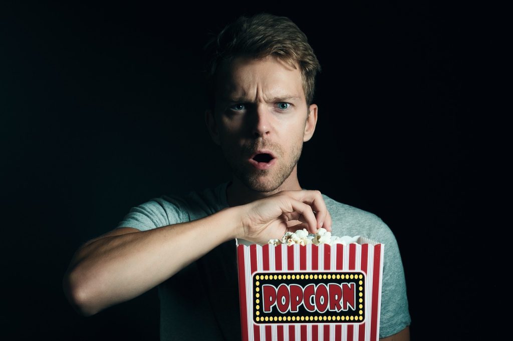 homme surpris tenant un bac de popcorn sur fond noir