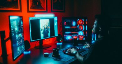 A young man working on a multi-screen computer setup in a dark, neon-lit room.