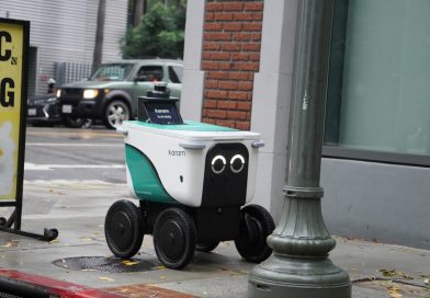 A small delivery robot with googly eyes on a sidewalk